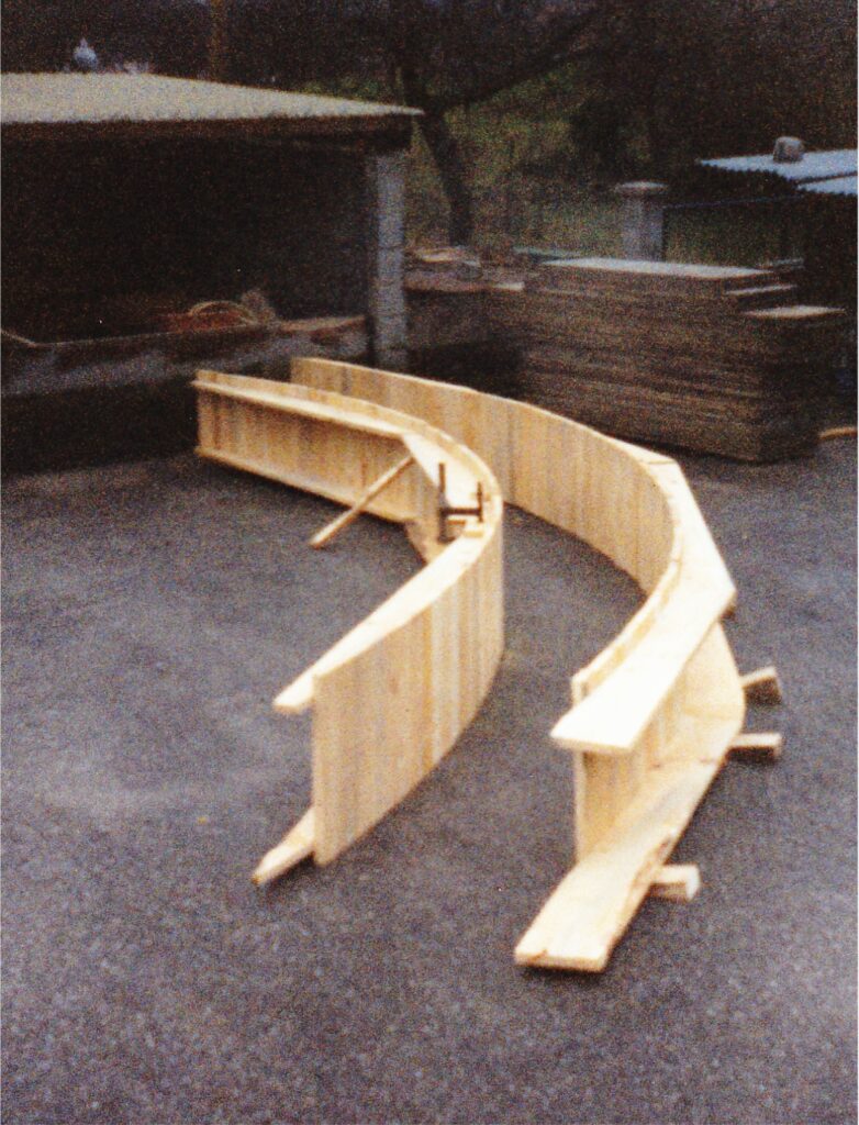Curved wooden formwork or hull mold made of vertical planks, outdoors in a workshop yard