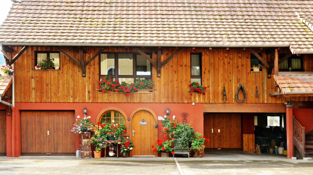 Timber storefront with a red base, window boxes of red geraniums and other plants along the facade.