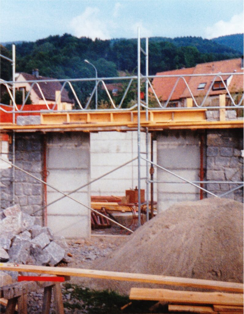 Construction site with concrete walls, scaffolding, and piles of dirt; wooden beams scattered around.