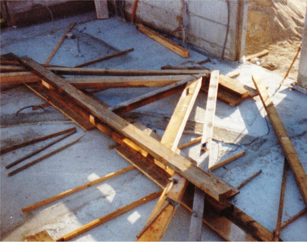 Construction debris scattered on a concrete floor with wooden planks and beams laying haphazardly.