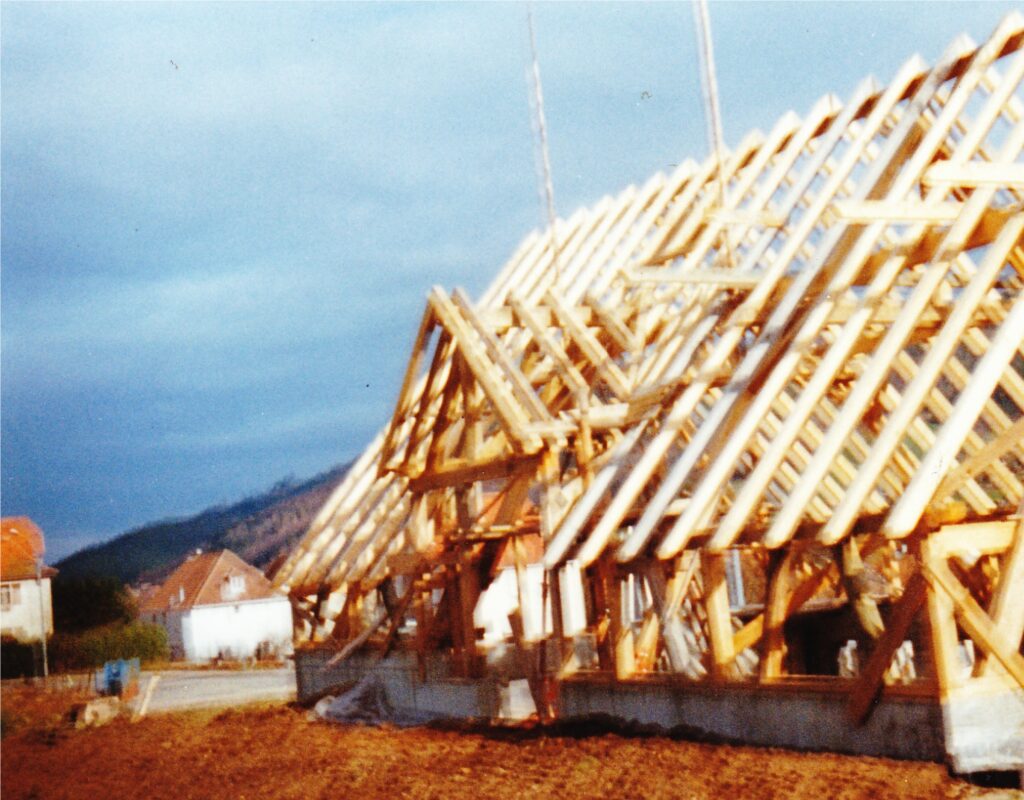Wooden roof trusses under construction beside a row of houses against a blue sky