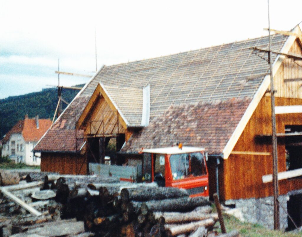 Construction site with a timber-framed house under construction, slate roof, and a red truck in front.
