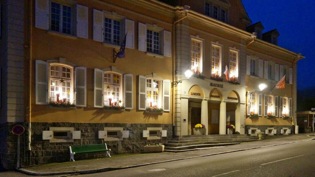 Nighttime view of a European town hall with arched entrance, columns, and warmly lit windows.