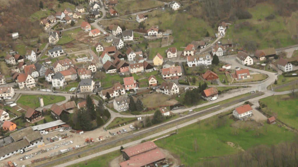 Aerial view of a small European village with colorful houses, winding streets and a railway line in the foreground.