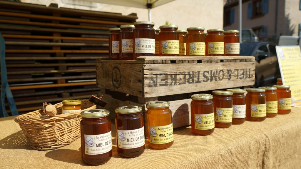 Row of glass honey jars on a rustic wooden crate at an outdoor market stall.
