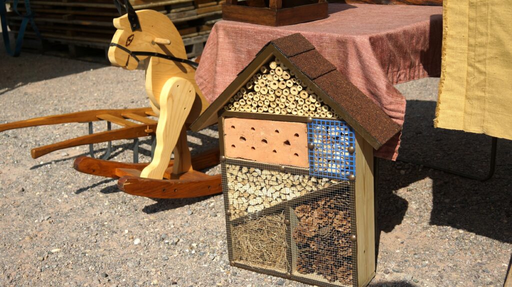 Beekeeping setup: a multi-chamber hive with visible honeycomb frames outdoors on gravel, next to a wooden horse figure.