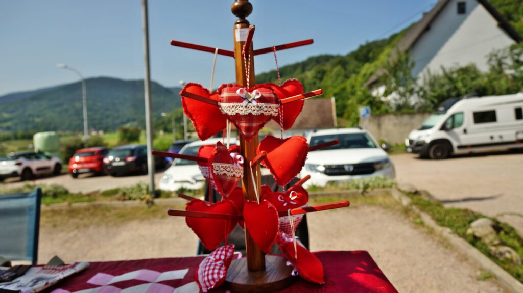 Heart-shaped fabric ornaments hanging on a wooden pole outdoors, likely a Valentine display with red and plaid ribbons.