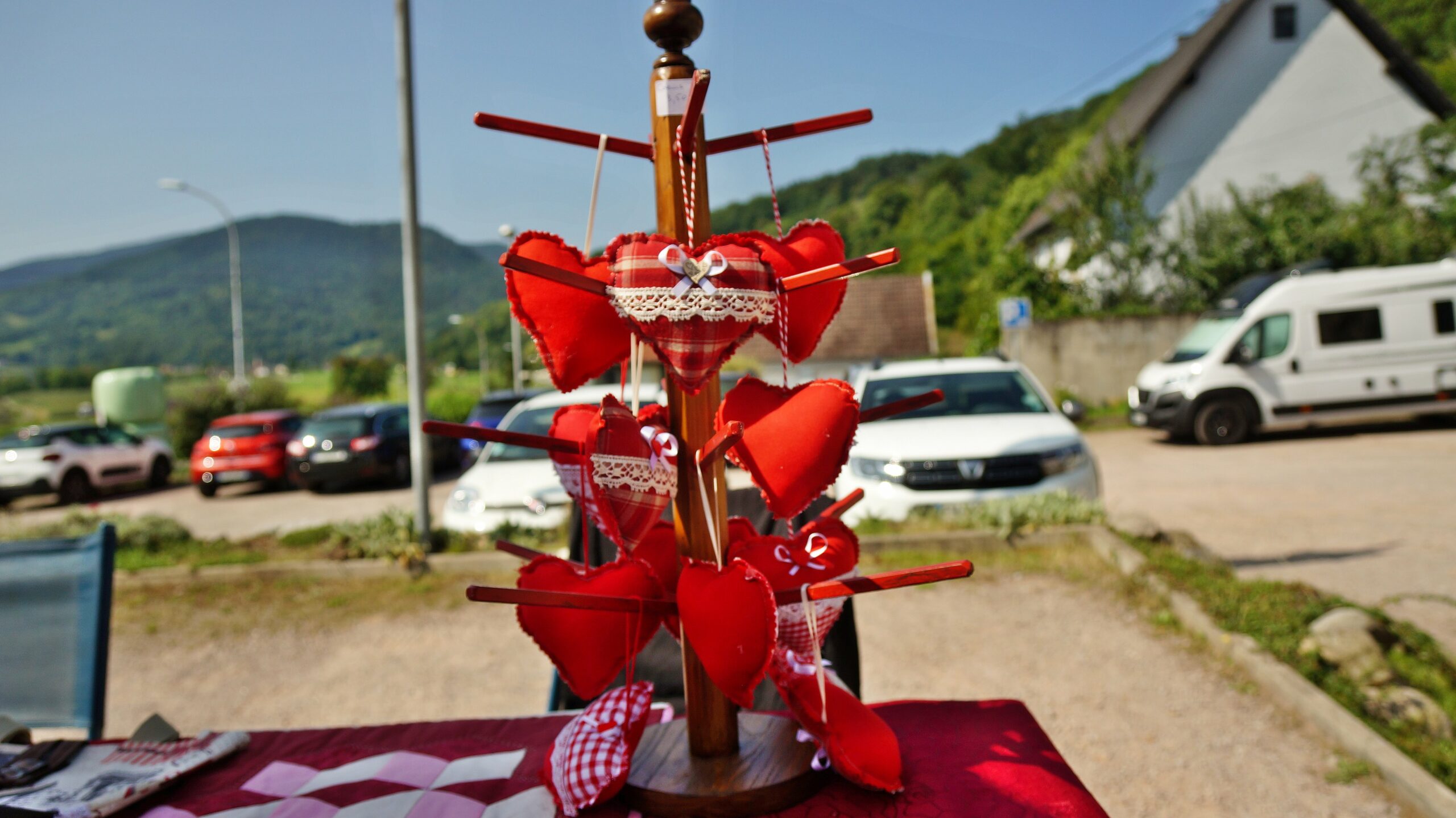 Heart-shaped fabric ornaments hanging on a wooden pole outdoors, likely a Valentine display with red and plaid ribbons.