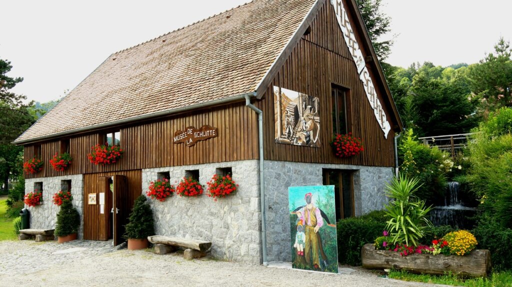 Chalet-style museum building with a stone base, wooden siding, and red flower baskets along the wall.