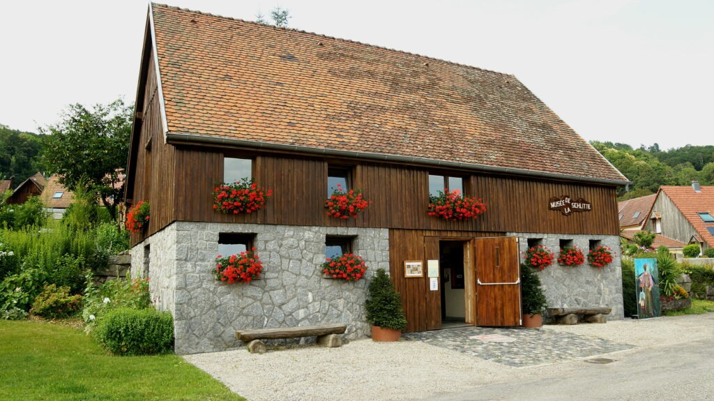 Wood-and-stone museum building with red flower boxes along the windows and an open entrance door.