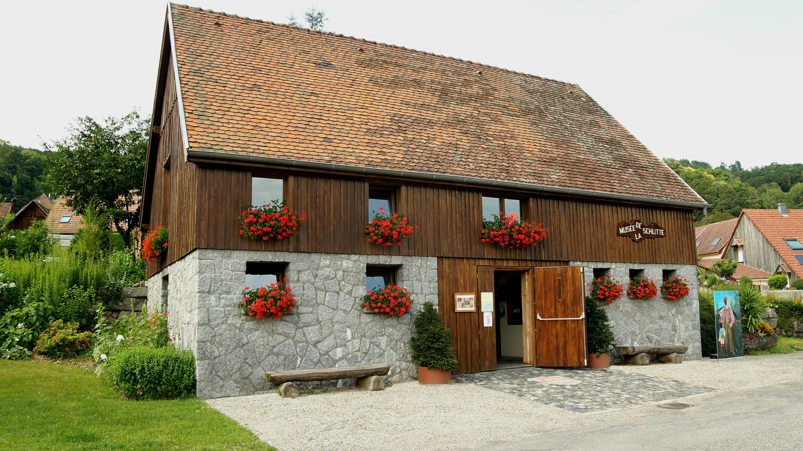 Wood-and-stone museum building with red flower boxes along the windows and an open entrance door.