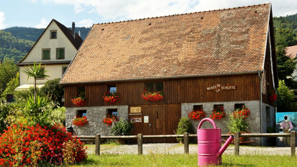Wooden museum building with a steep red-tiled roof and flower-filled windows on a sunny day in the countryside
