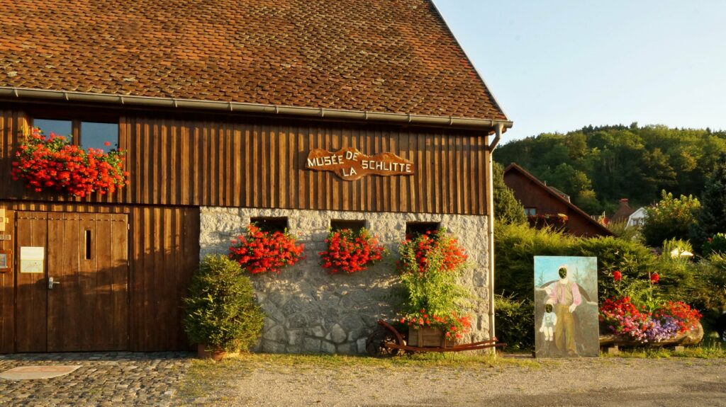 Wooden museum building with red flower boxes along the wall and a sign reading 'Musée de la Schlitte'