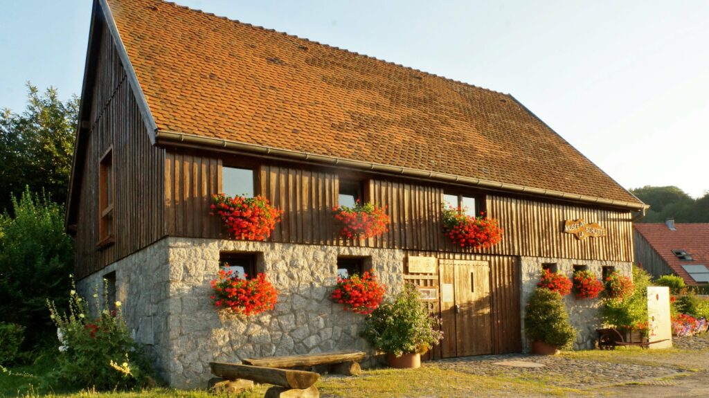 Rustic wooden museum building with a stone base, a long red-tiled roof, and red flower boxes along the balcony railing on both levels.