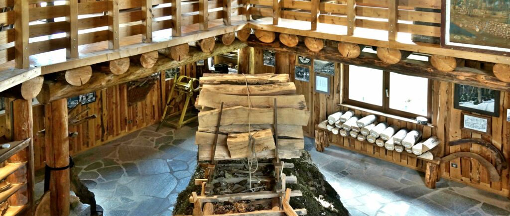Interior of a rustic log cabin museum with a mezzanine balcony, large round logs, and framed displays along a stone floor.